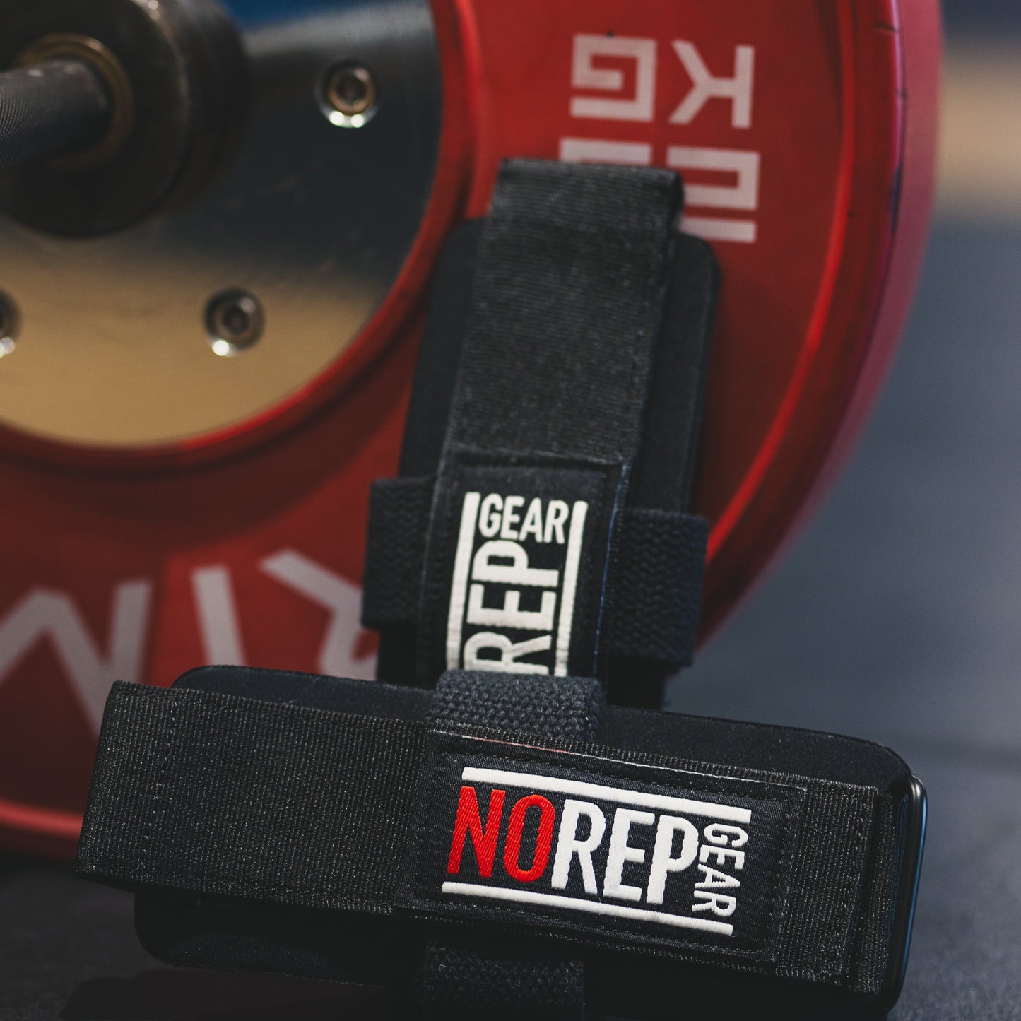 Black weightlifting strap with 'NO REP GEAR' branding in front of a red weight plate.