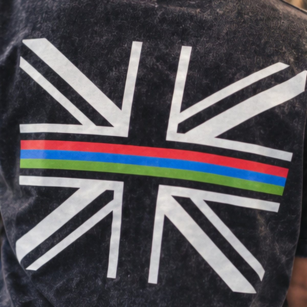 Close-up of the back of a person wearing a dark washed T-shirt with a large white Union Jack-style graphic and a horizontal multicolor stripe across the center.