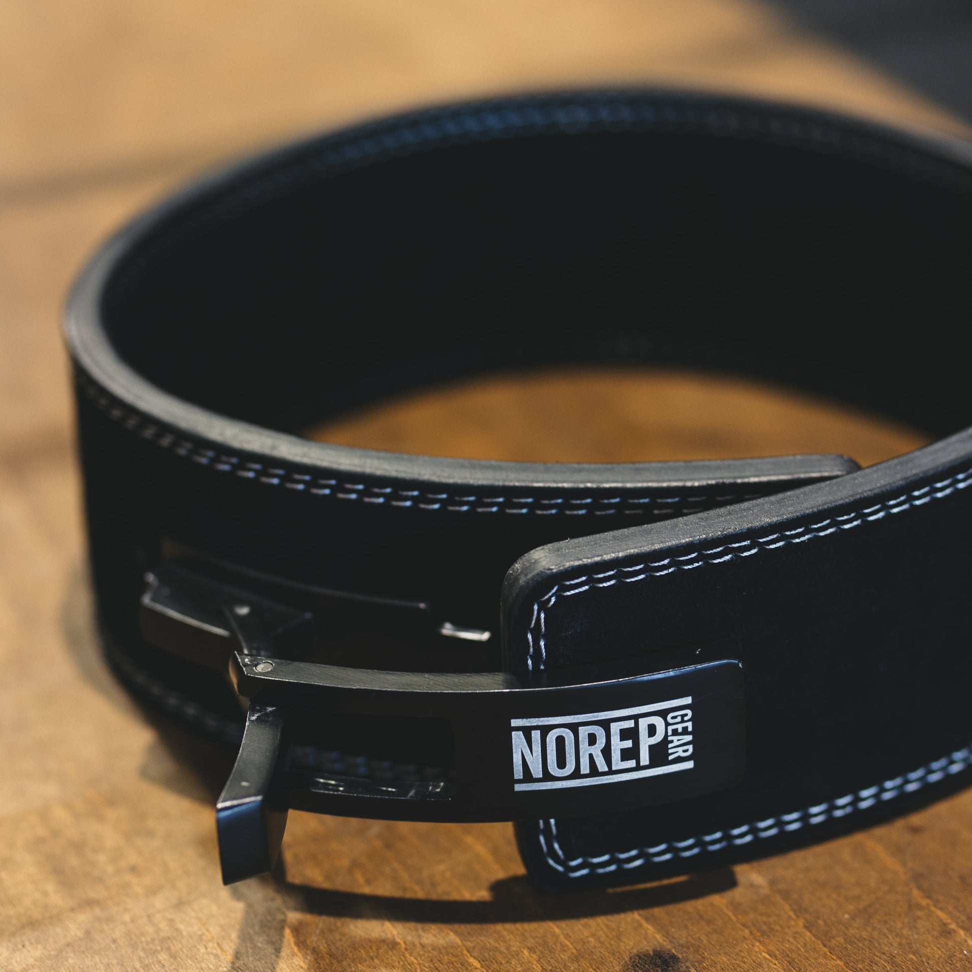 Black leather belt with a visible brand label on a wooden surface