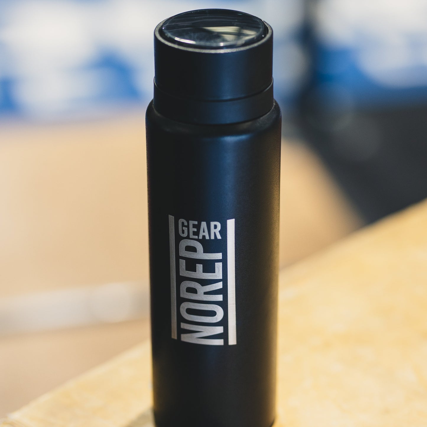 Black water bottle with 'NOREP GEAR' branding on a wooden surface.