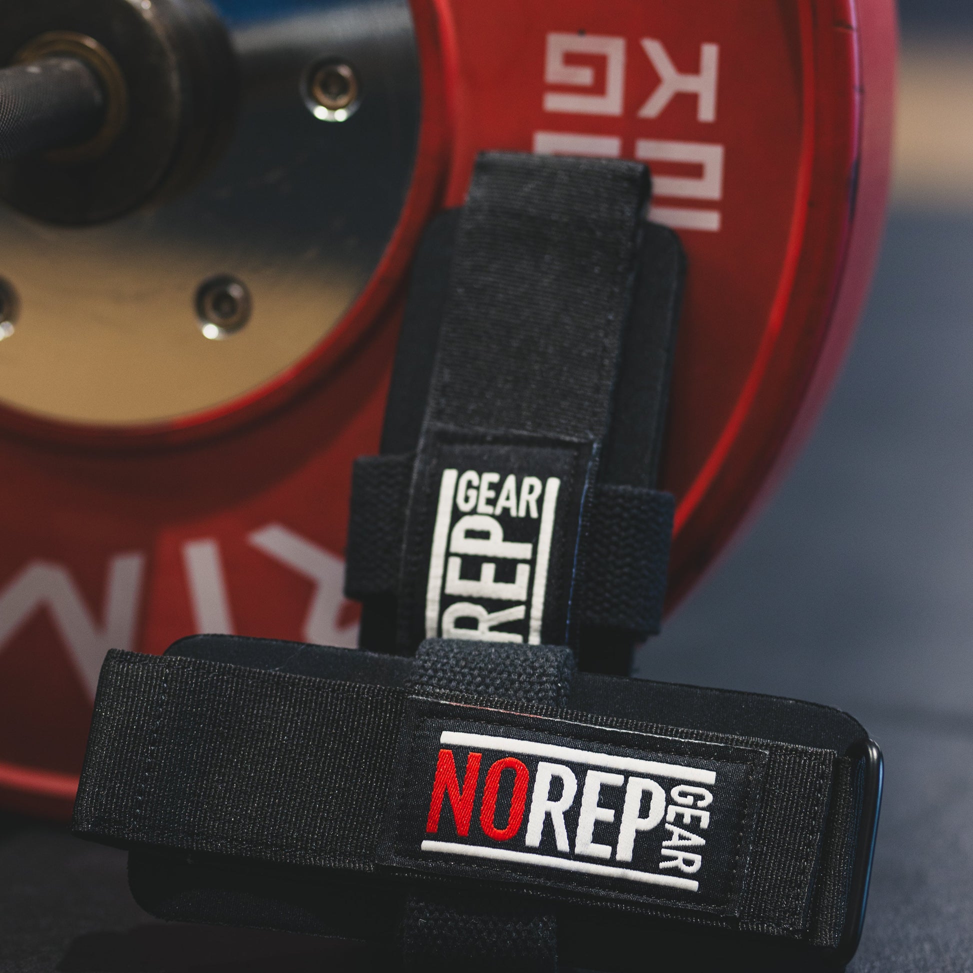 Black weightlifting strap with 'NO REP GEAR' branding in front of a red weight plate.